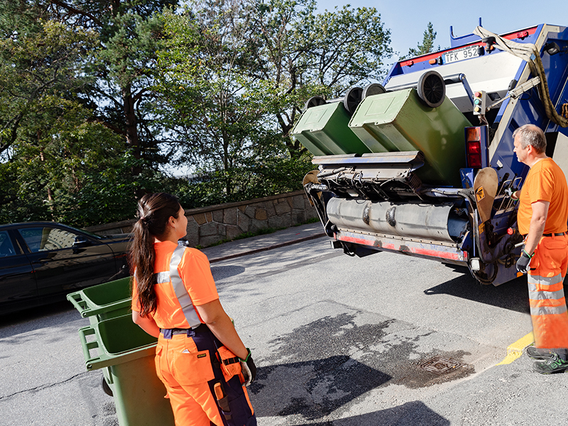 Kvinnlig och manlig sophämtare vid sopbil